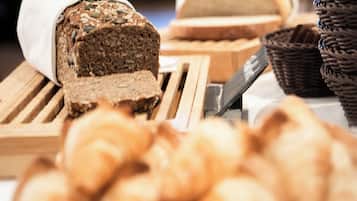 A loaf of bread with seeds on a wooden board, a knife, and several baskets of bread.