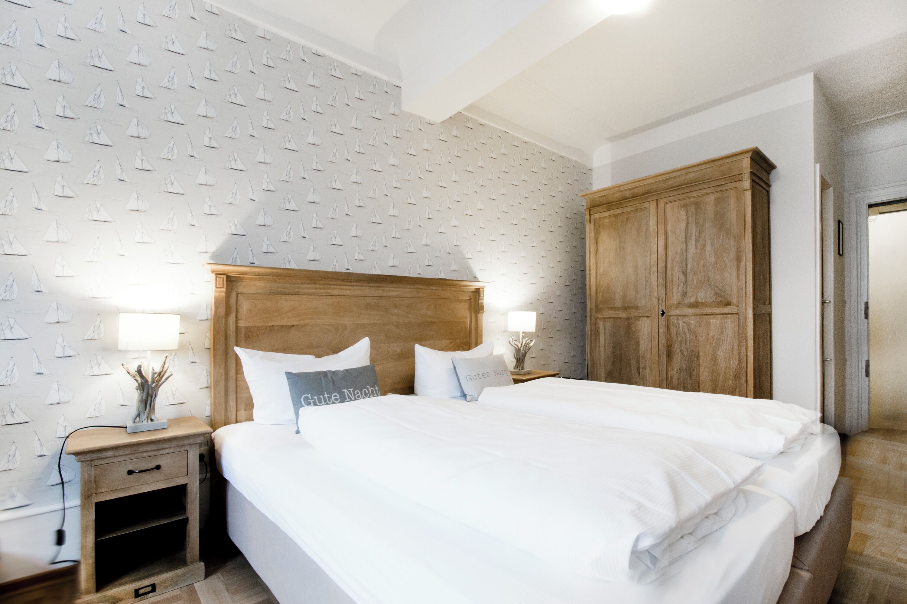 A neatly made bed with white linens, a wooden headboard, and two bedside lamps.