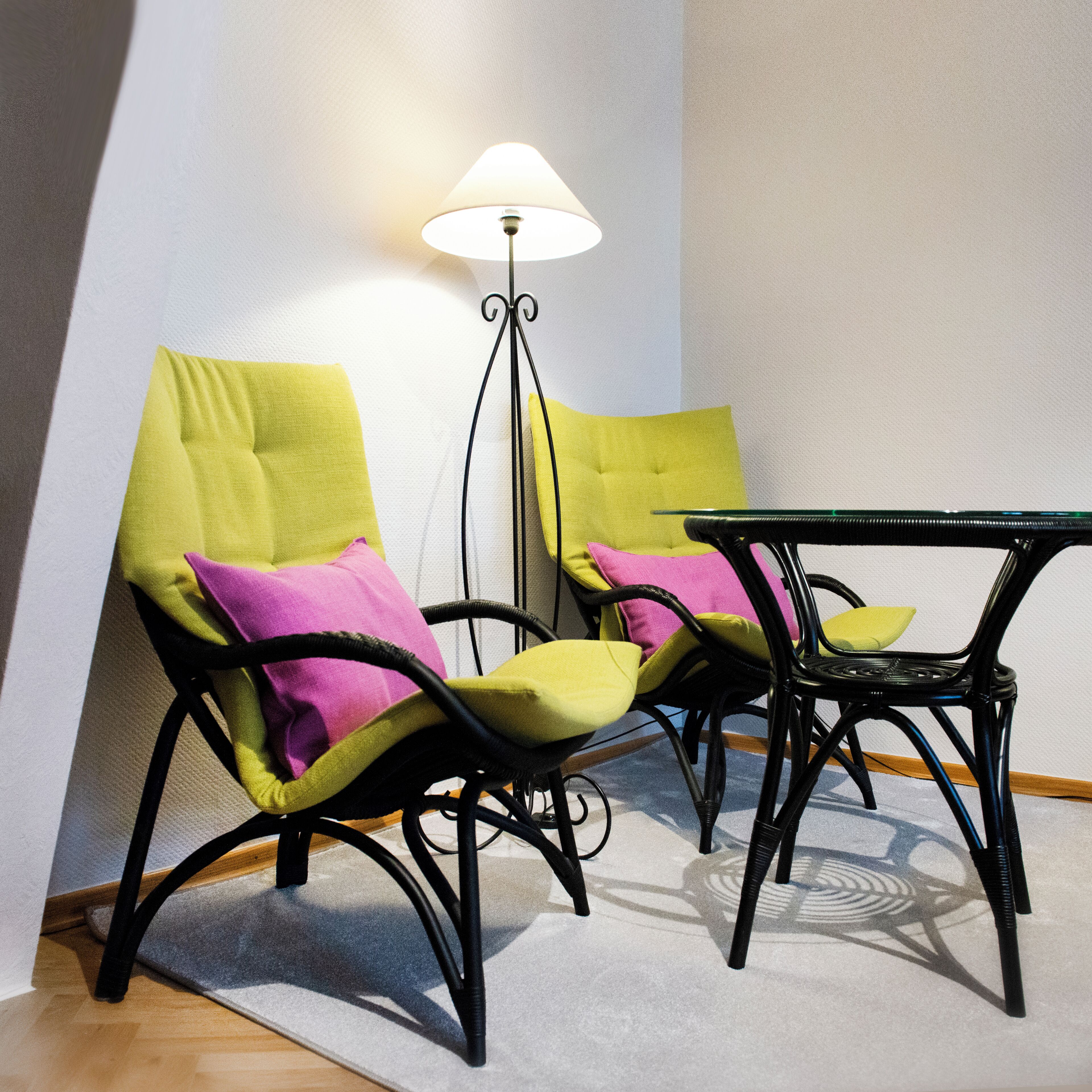 A room with two black chairs with yellow and pink cushions, a small black table, and a floor lamp.