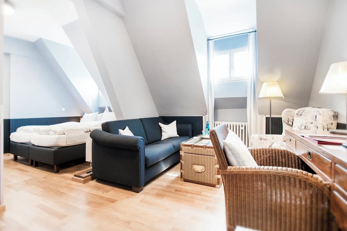 A modern loft bedroom with a dark blue sofa, a white bed, and a wicker chair.