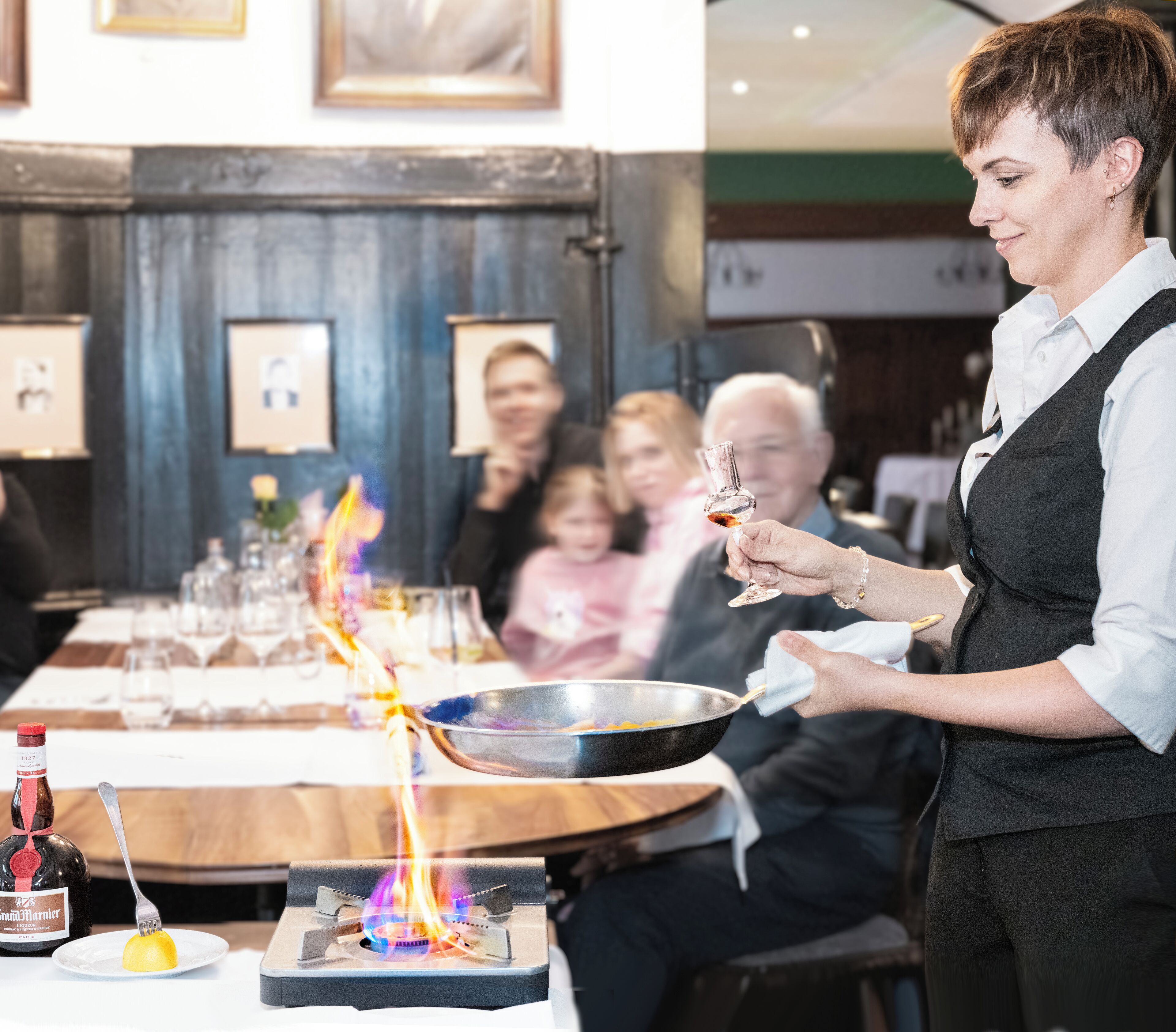 A person serving food at a table with a lit stove in the background.