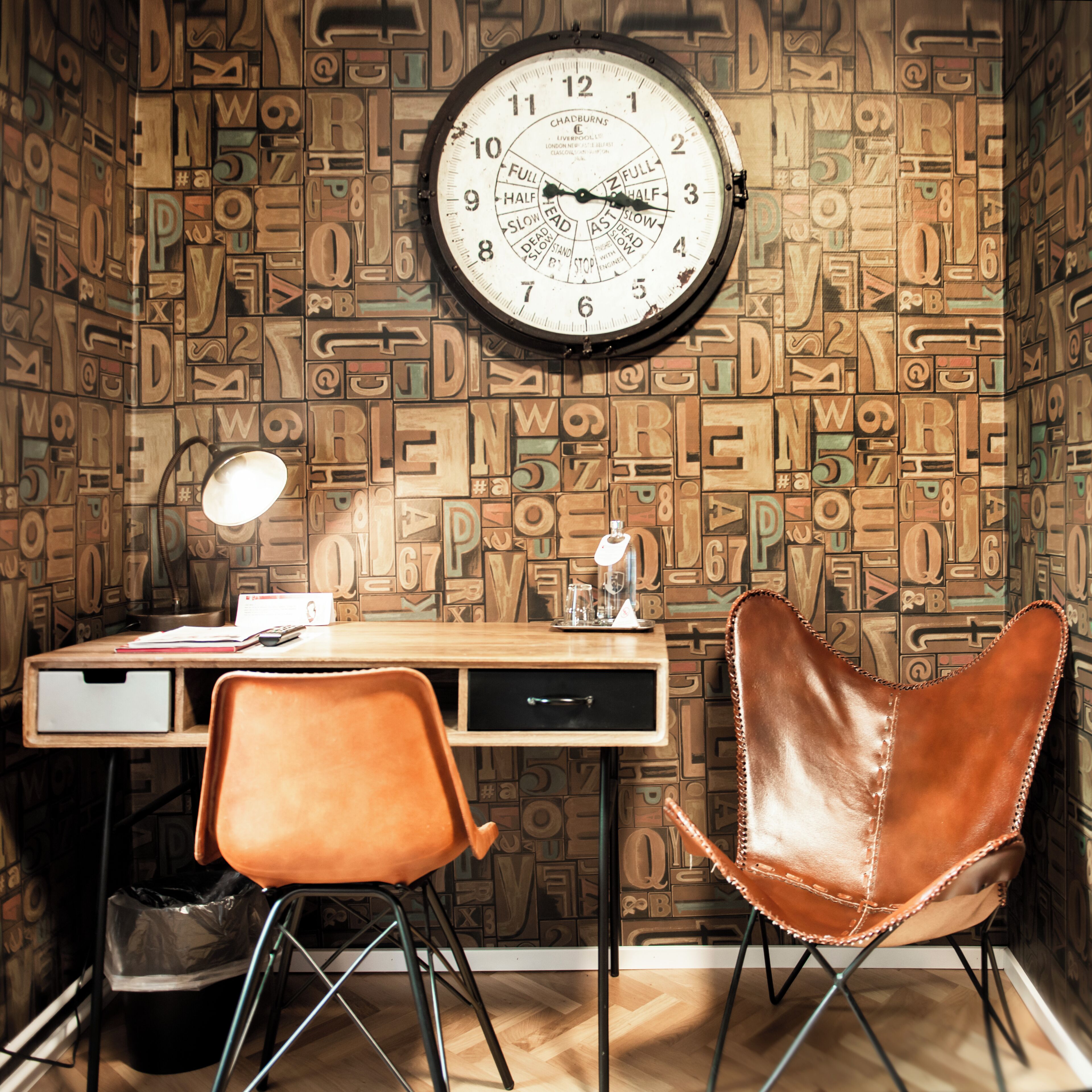 Ein Zimmer mit einem Holztisch, einem Ledersessel, einer Wanduhr und einem Mülleimer.