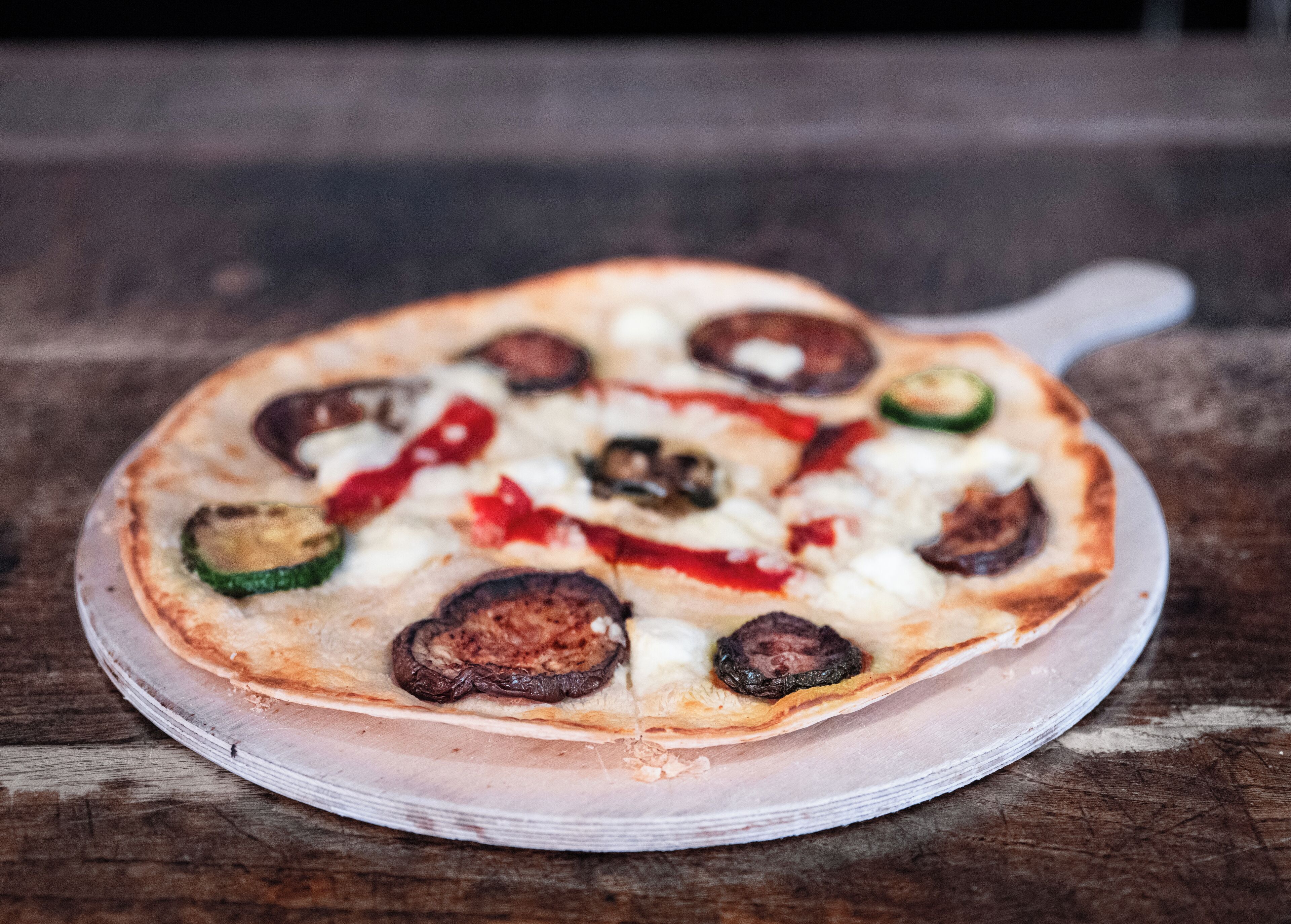 A pizza on a clear glass plate on a wooden surface.