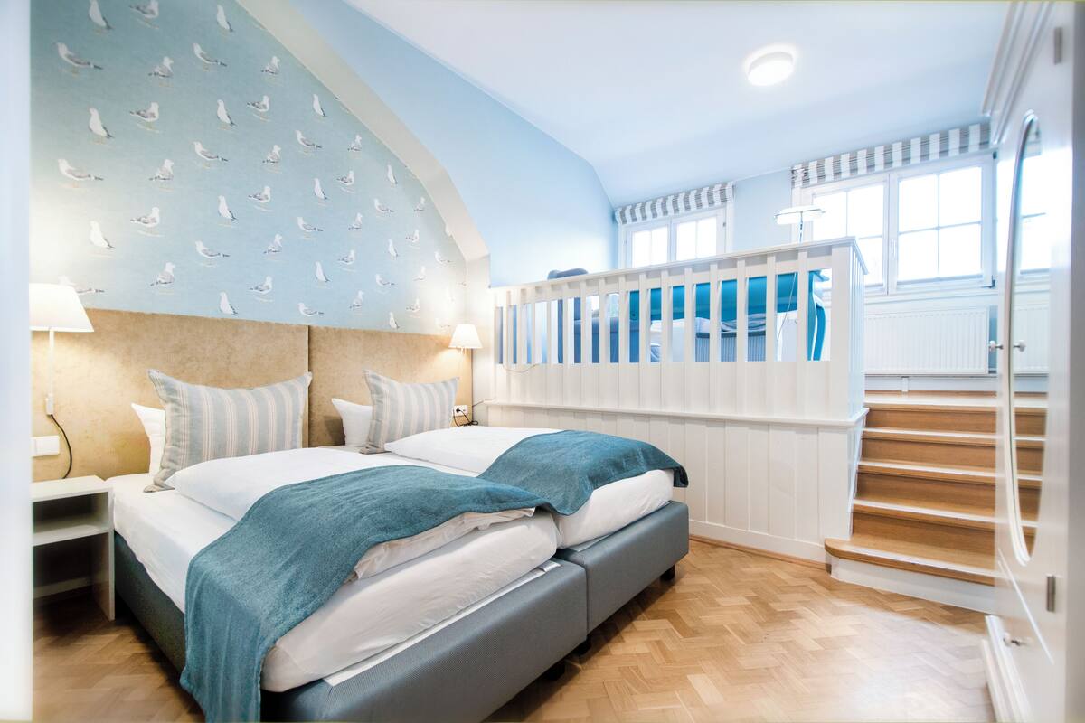 A bedroom with a bed, two bedside tables, a nightstand, a window, and a staircase.