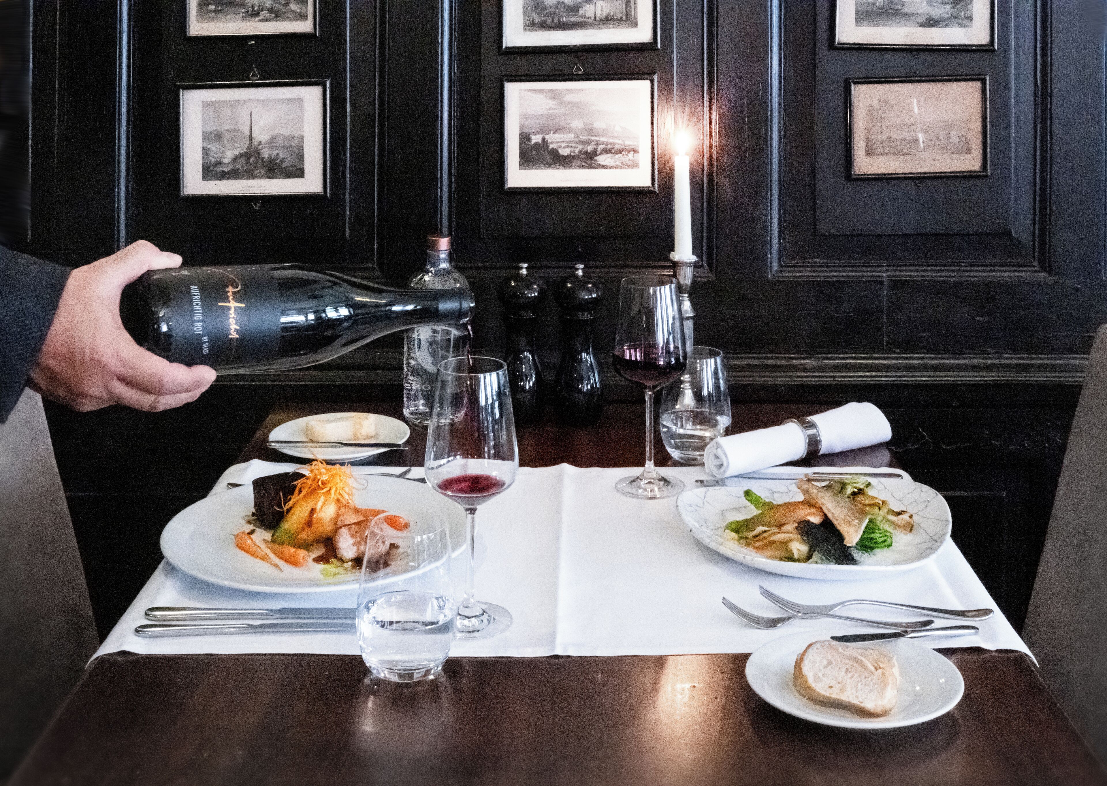 A table set for a meal with plates of food, glasses of water and wine, and a bottle being poured.