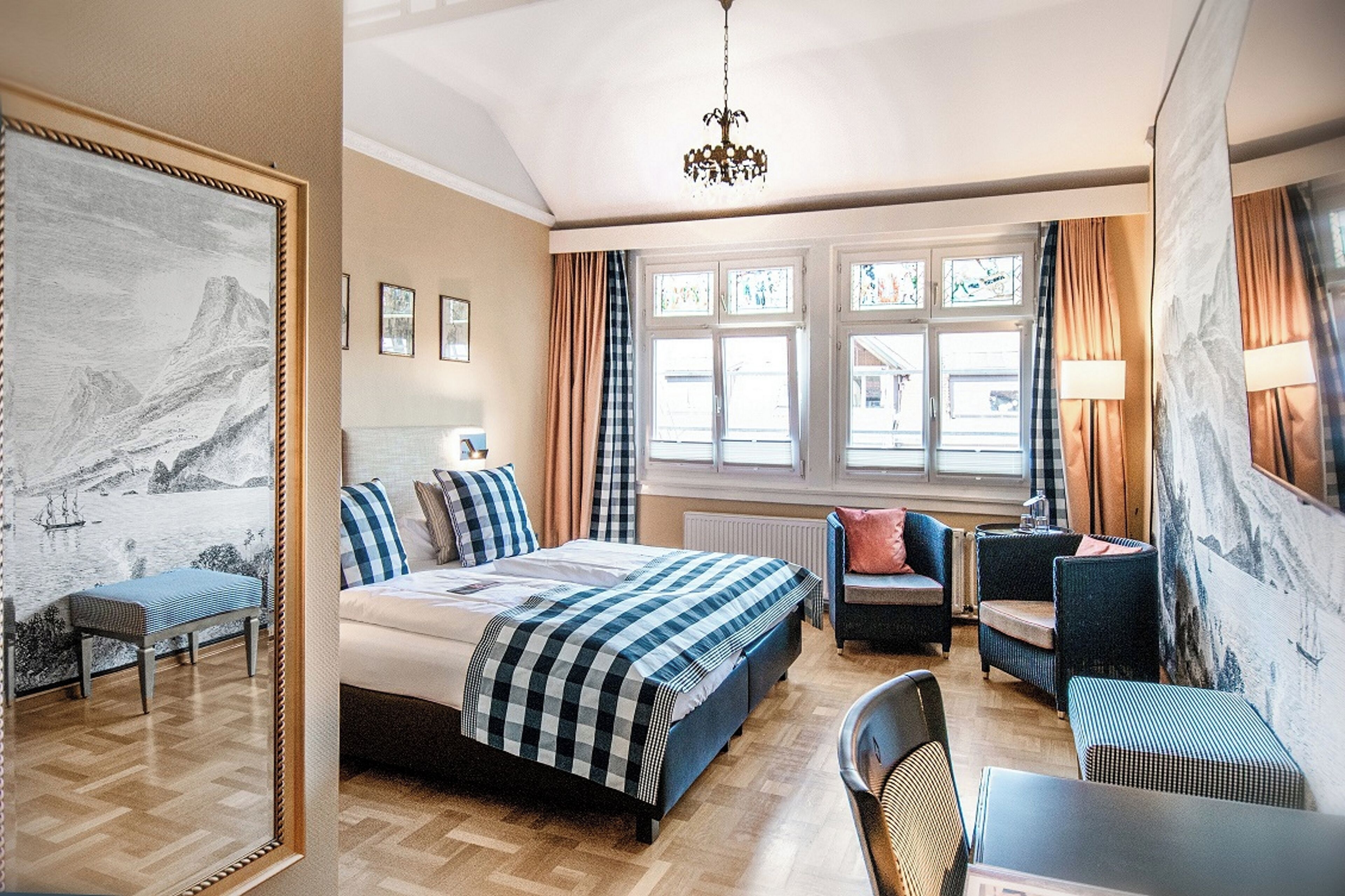 Ein Hotelzimmer mit einem Bett, einer Sitzecke mit Sesseln, einem Tisch, einem großen Fenster mit Vorhängen und Kunstwerken an den Wänden.