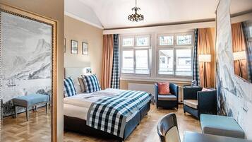 Ein Hotelzimmer mit einem Bett, einer Sitzecke mit Sesseln, einem Tisch, einem großen Fenster mit Vorhängen und Kunstwerken an den Wänden.