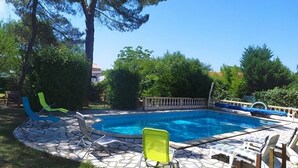 Une piscine entourée de chaises longues, d’une terrasse en pierre et d’une végétation luxuriante.