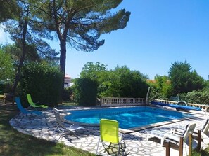 Une piscine entourée de chaises longues, d’une terrasse en pierre et d’une végétation luxuriante.