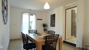 Un coin repas avec une table en bois, quatre chaises, une plante en pot et un panneau mural indiquant une liste de villes.