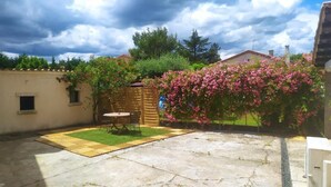 Un jardin avec une terrasse en pierre, une clôture en bois et des plantes fleuries.