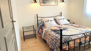 Une chambre à coucher bien rangée, avec un lit en métal, une table de chevet, une lampe fixée au mur et un tableau encadré.