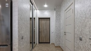 Un pasillo con un refrigerador, una puerta de madera y una puerta blanca con manijas horizontales.