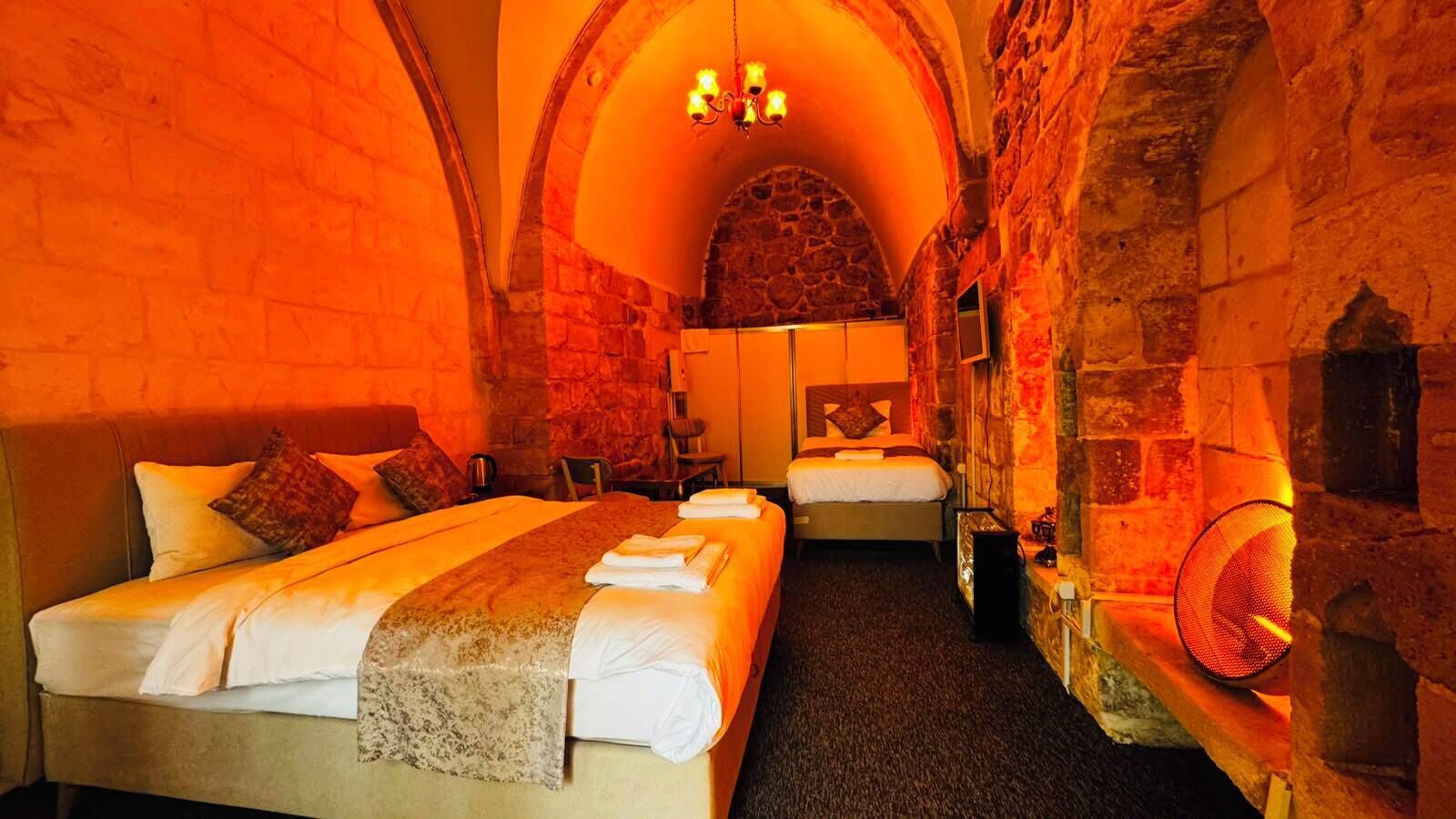 Habitación de hotel con pared de piedra, una cama, otra cama, chimenea y un candelabro.