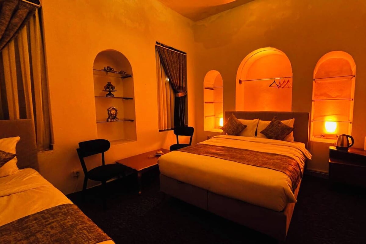 A hotel room with a bed, a desk, a chair, and a nightstand with a lamp.