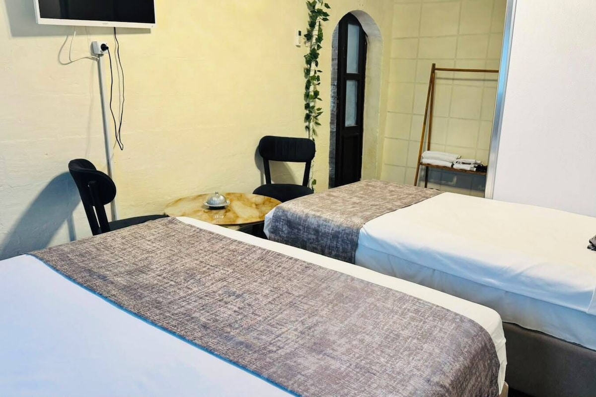 A room with two beds, a desk, a chair, and a TV mounted on the wall.