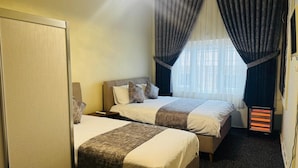 A hotel room with two beds, a heater, and a window with curtains. - Tunç Paşa Konağı (Mardin)