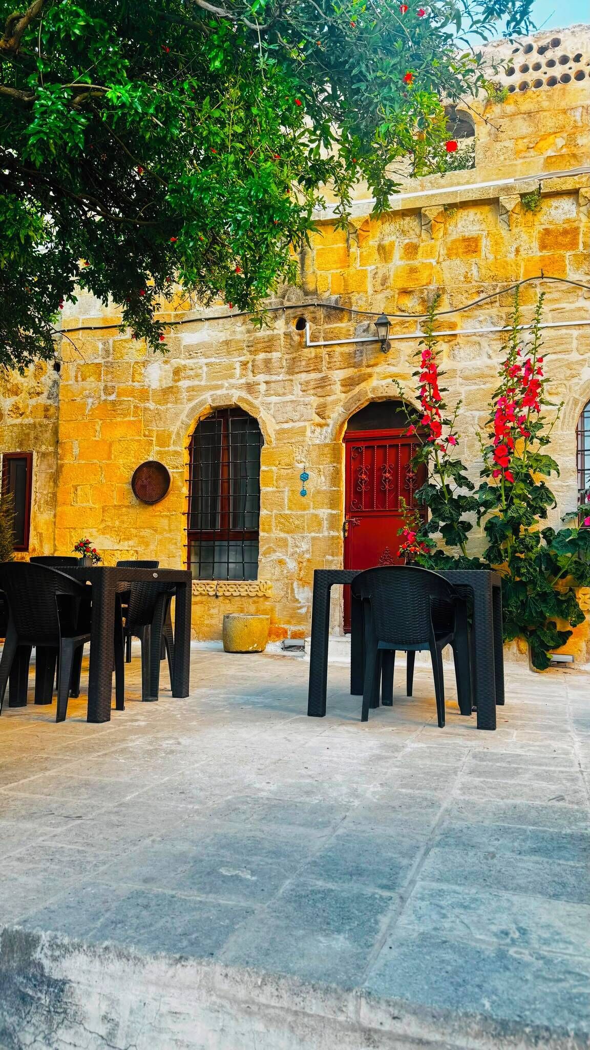 An outdoor seating area with stone walls and a red door, featuring outdoor furniture and potted plants.