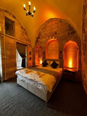 A bedroom with a stone wall, a bed, and a chandelier. - Tunç Paşa Konağı (Mardin)
