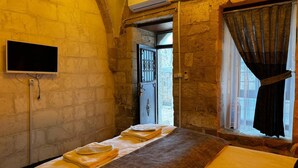 A room with a bed, a TV, and a window with curtains. - Tunç Paşa Konağı (Mardin)
