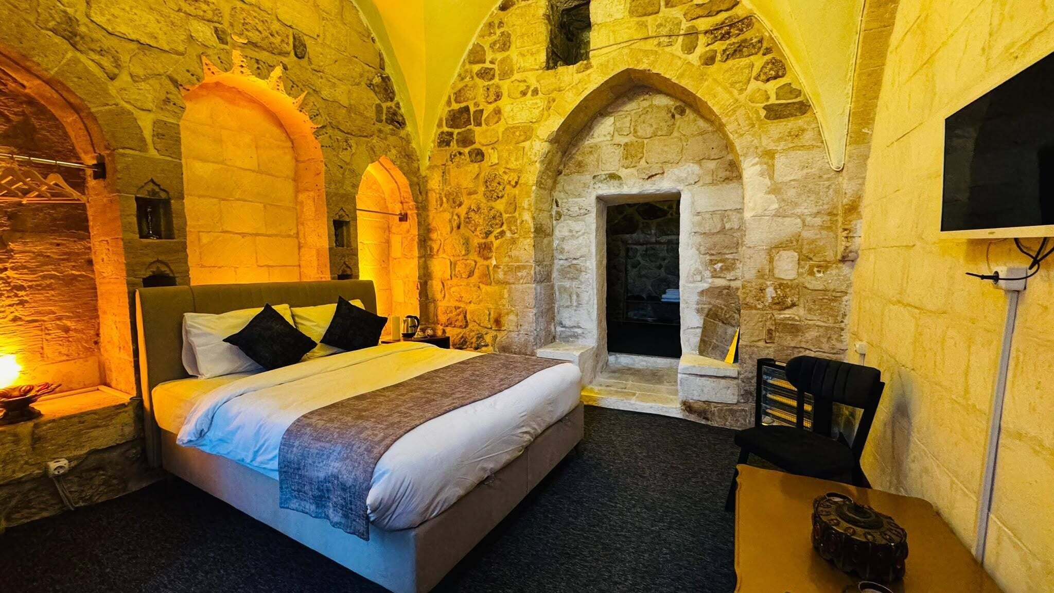 Un dormitorio con pared de piedra, una cama, un televisor y una chimenea.
