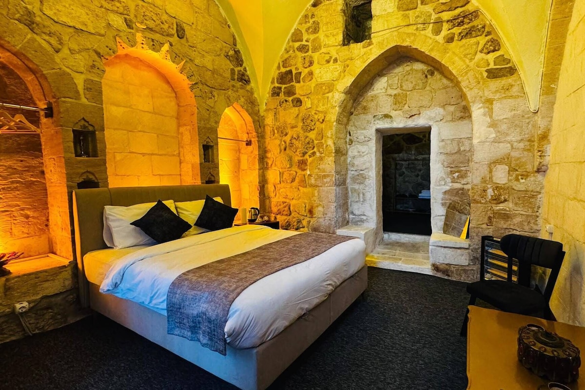 A bedroom with a stone wall, a bed, a television, and a fireplace.