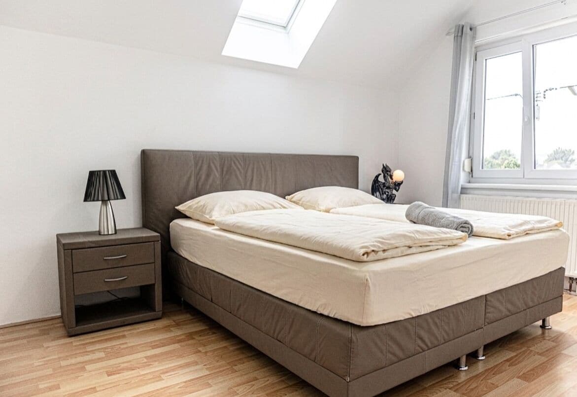 A bedroom with a bed, a nightstand, a lamp, and a window.