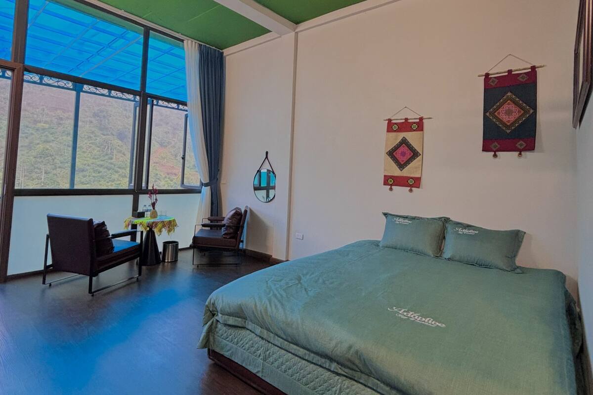 A bedroom with a large bed, a desk, a chair, and a view of the outdoors.