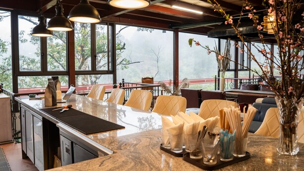 A restaurant with a marble counter, cushioned chairs, and large windows offering a view of trees. - The Legend of Dragon Tea Suoi Giang  (Van Chan)