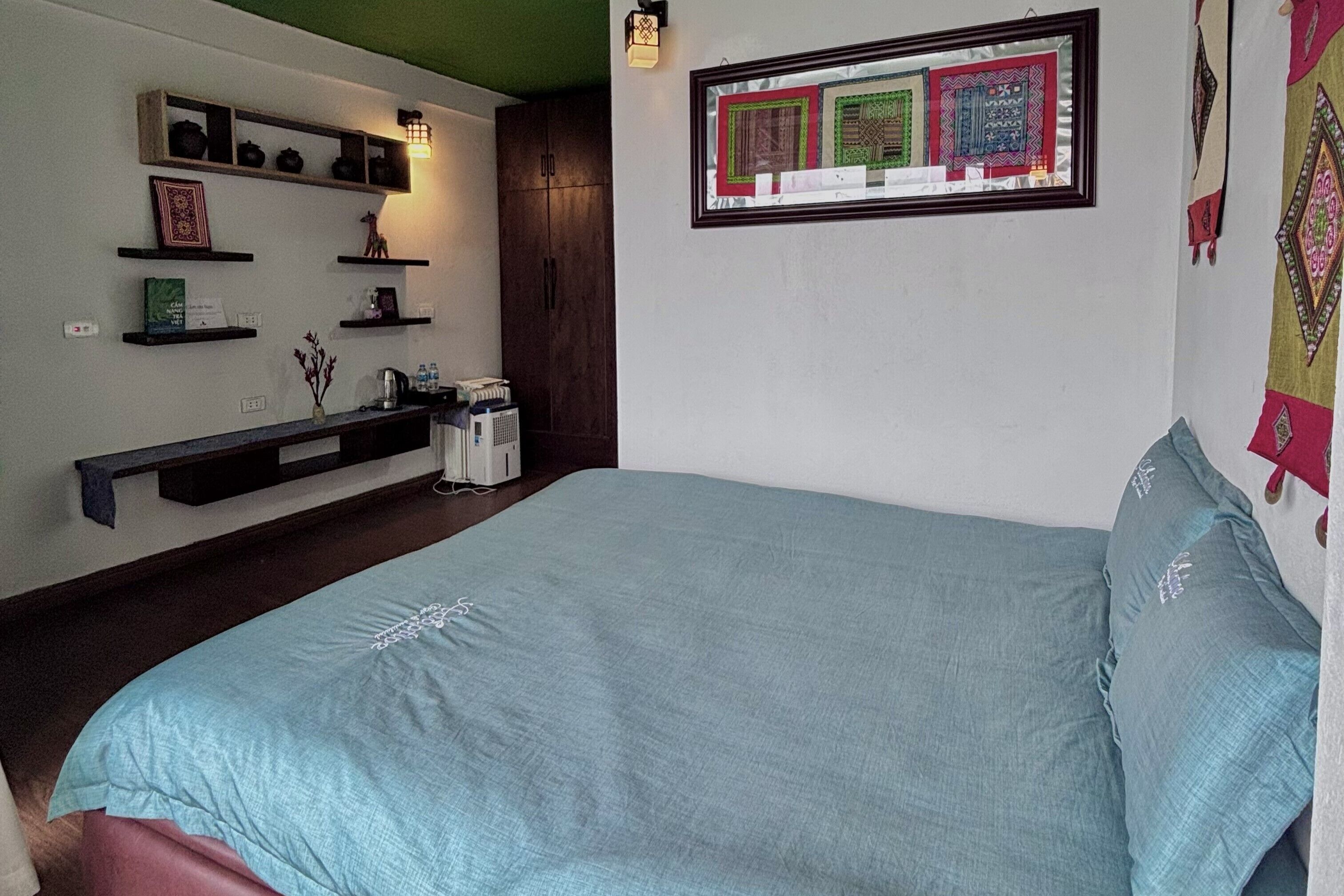 Ein Schlafzimmer mit einem Bett, einem Nachttisch, einem Regal mit Dekoration und einem an der Wand hängenden Bilderrahmen.