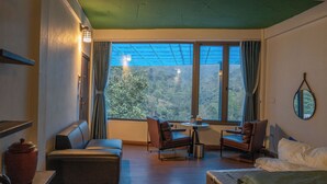 A room with a sofa, two armchairs, a small table, and a bed. There is a large window with curtains and a view of a forested area. - The Legend of Dragon Tea Suoi Giang  (Van Chan)