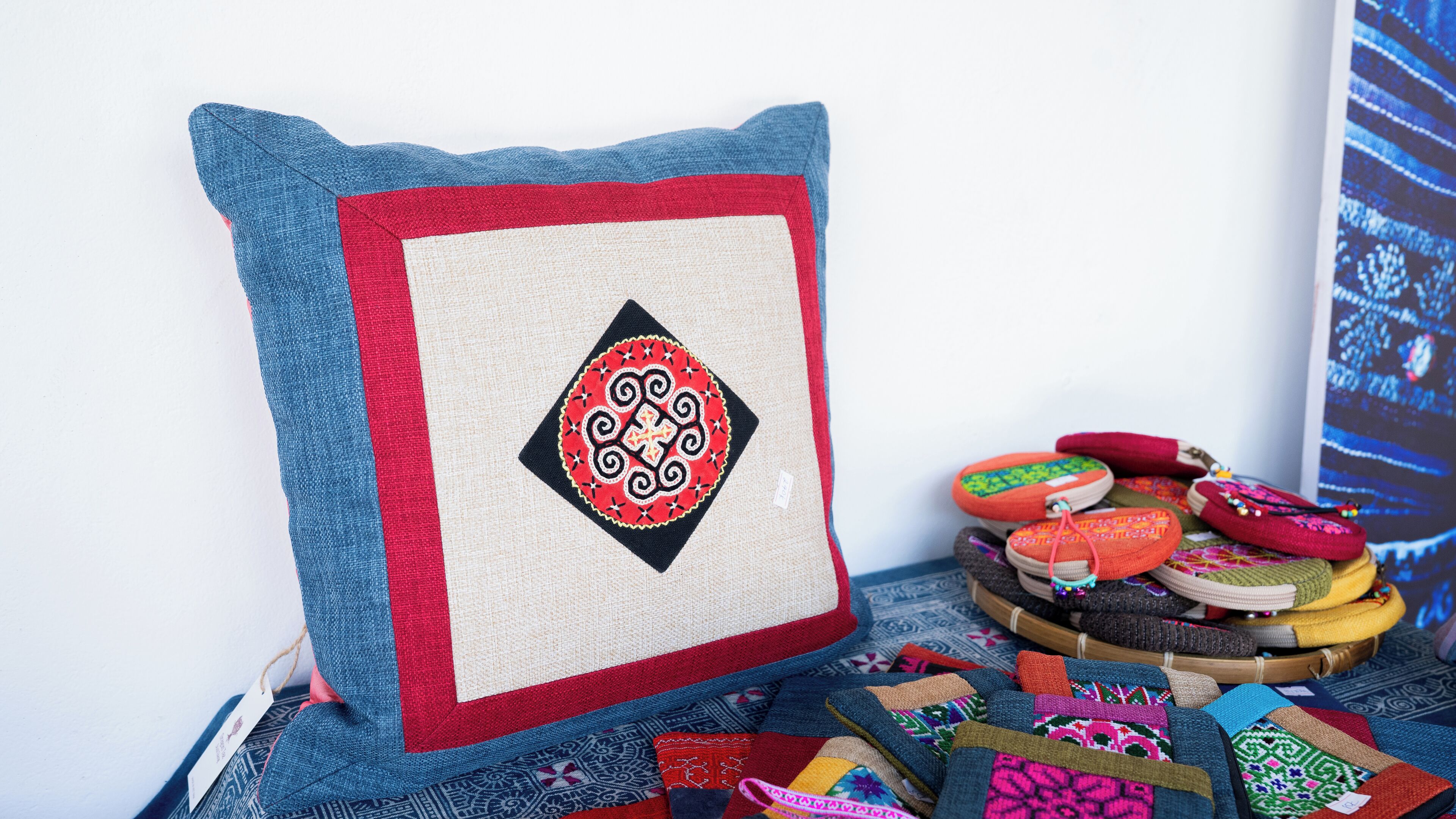 Un cojín con estampado geométrico, una pila de bolsas tejidas de colores y una variedad de textiles.