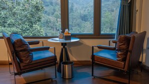 A room with two leather chairs, a small table with a tissue box and a candle, and a window with a view of a forest. - The Legend of Dragon Tea Suoi Giang  (Van Chan)