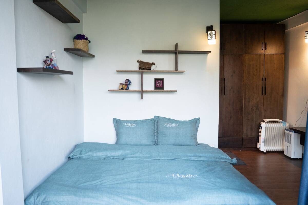 A bedroom with a bed, a wall-mounted shelf with decorative items, a radiator, and a wardrobe.