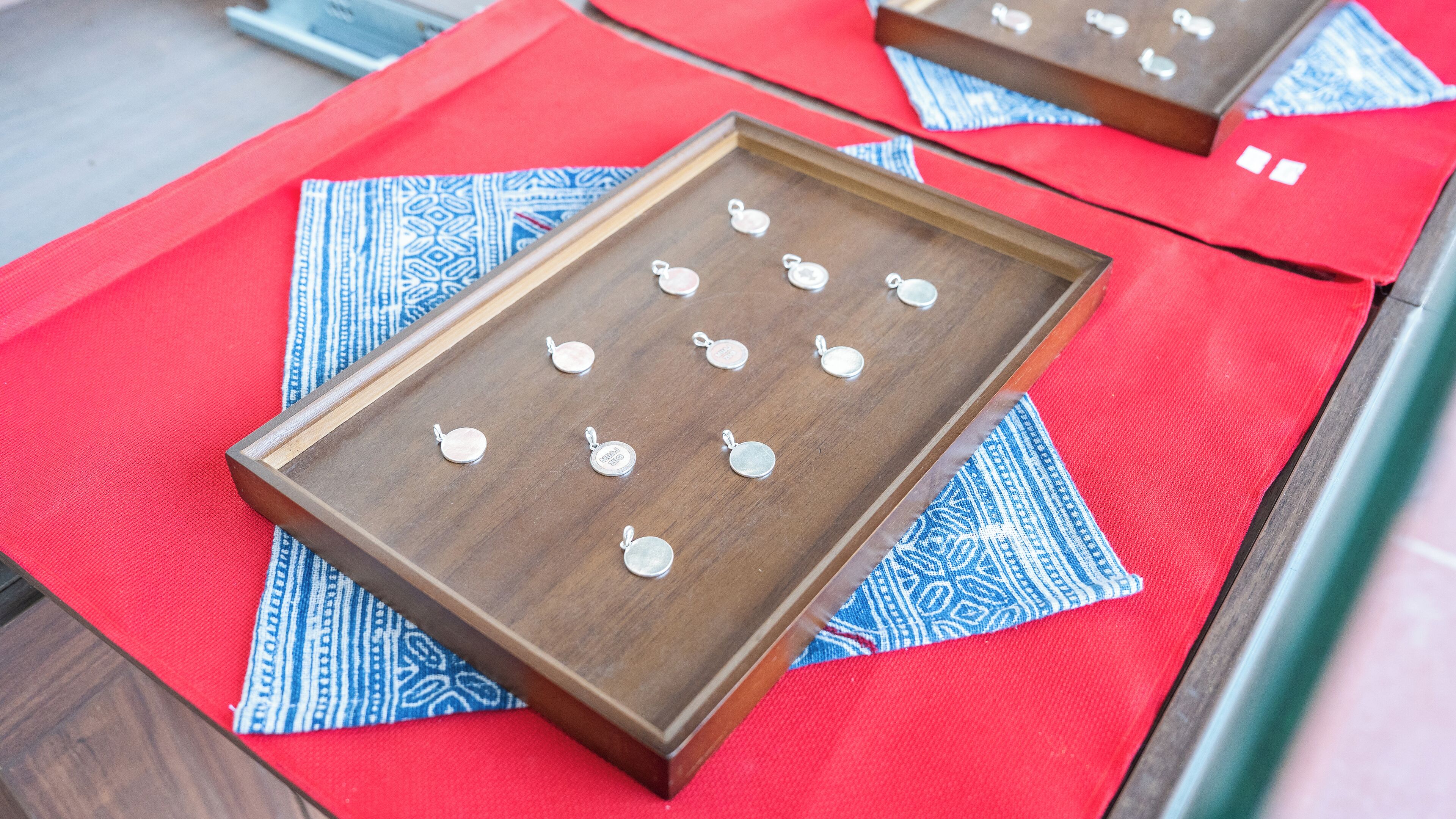 A wooden tray with several silver pendants on a red fabric surface.