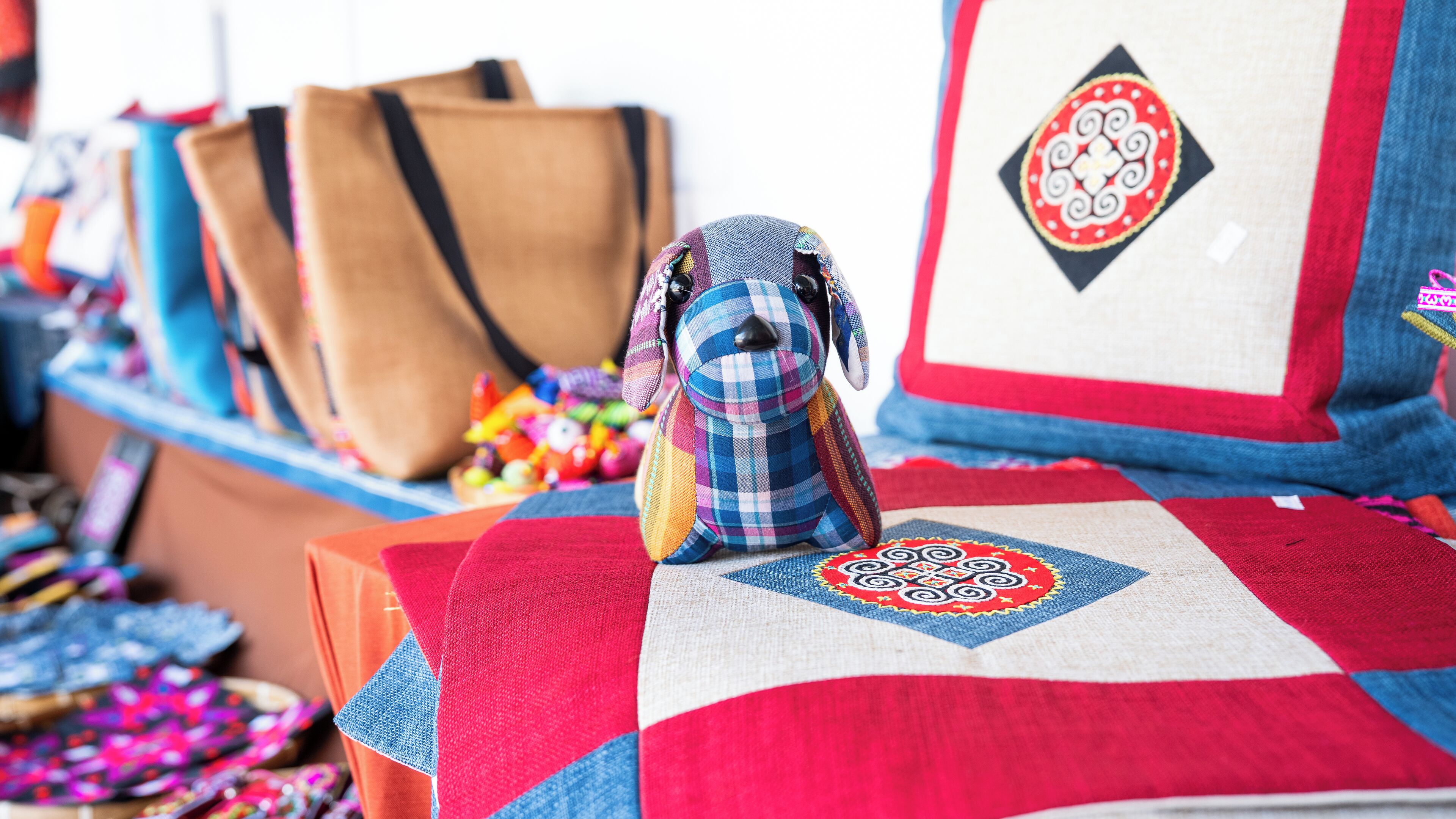Un colcha colorida con un diseño geométrico, una figurita de perro pequeño y un bolso marrón al fondo.