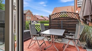 Eine Terrasse im Freien mit Tisch und Stühlen, einem Holzzaun und Blick auf Wohnhäuser.