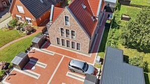 Ein Wohngebäude mit Parkplatz, einem Auto und einem gepflegten Garten.