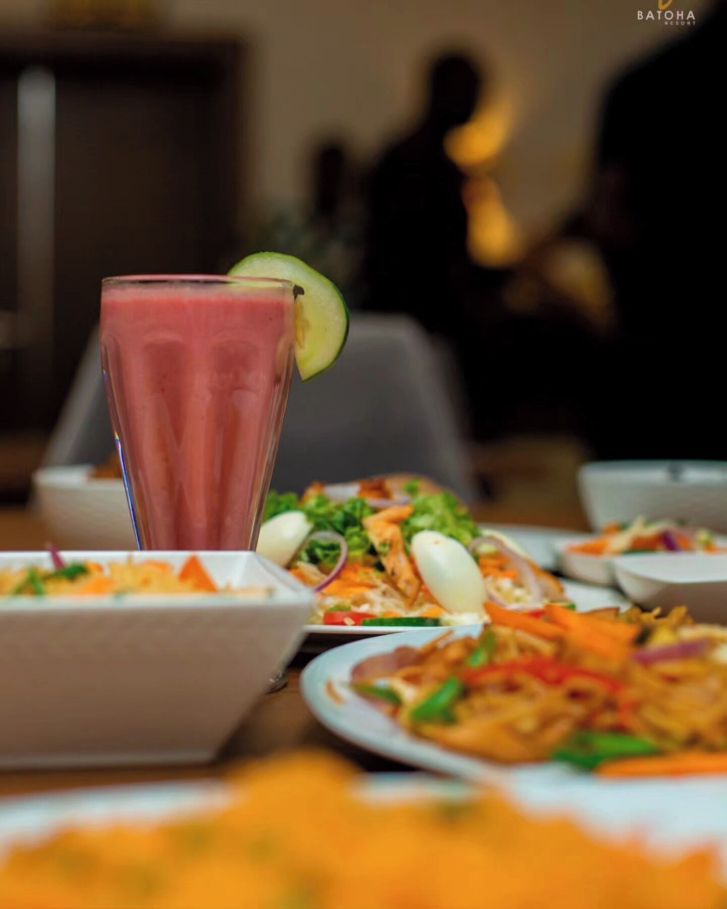 A dining table with various dishes and a glass of a pink beverage with a lime garnish.
