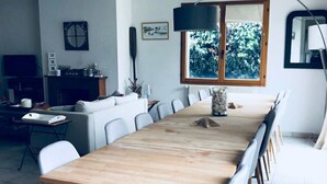 A modern dining area with a long wooden table, grey upholstered chairs, and a large window with a view of greenery. - Maison KER HEOL (first floor only) 100 m from the beach on the bay side (Saint-Pierre-Quiberon)