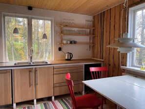 Eine Küche mit Holzausstattung, einer weißen Arbeitsplatte, einem roten Stuhl und einem Fenster mit Blick auf Bäume.