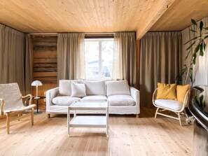 A living room with a white sofa, a white coffee table, a wooden floor, and a window with curtains.