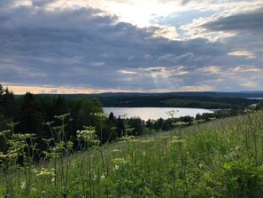 Un paysage naturel comprenant un lac, des collines boisées et un ciel nuageux.