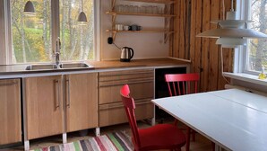 Eine Küche mit Holzausstattung, einem Spülbecken, einem Wasserkocher und einem roten Stuhl. Über der Arbeitsplatte befinden sich Regale mit Gläsern und Tassen.