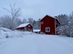 Et rødt træhus med et sneklædt tag og en mindre tilbygning.