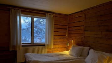 Ein Zimmer mit einem Bett, einem Vorhangfenster, einem Heizkörper und Holzwänden.