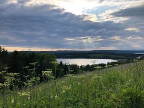 Un paisaje natural con un lago, colinas boscosas y un cielo nublado.