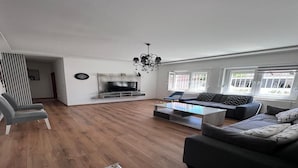 A spacious living room with a large TV, comfortable seating, and a chandelier. - Spacious 3-Bedroom, 2-Bath Apartment in Ilidža – Near Airport, Garden & BBQ (Ilidža)