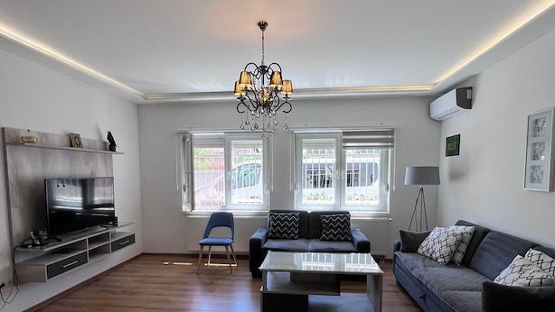 A spacious living room with a flat-screen TV, a modern chandelier, a sofa, and a coffee table. - Spacious 3-Bedroom, 2-Bath Apartment in Ilidža – Near Airport, Garden & BBQ (Ilidža)