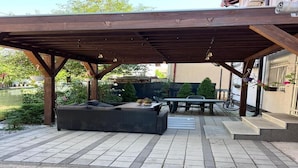 A covered patio area with a wooden pergola, a sofa, a table, and a bicycle. - Spacious 3-Bedroom, 2-Bath Apartment in Ilidža – Near Airport, Garden & BBQ (Ilidža)